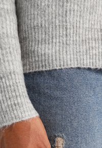 Szary dzianinowy sweter prążkowany o miękkiej fakturze, zestawiony z niebieskim, postrzępionym denimm z widoczną kieszenią.