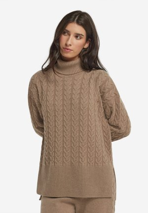Pull en maille cable beige avec un col roulé et un ourlet côtelés. Il présente une coupe ample et un motif texturé, idéal pour le superposition.