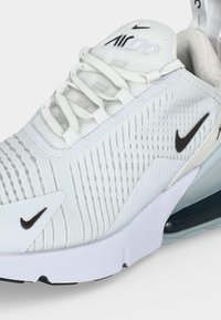 Κοντινό πλάνο λευκού αθλητικού παπουτσιού Nike Air 270 με μαύρα λογότυπα swoosh, διχτυωτό επάνω μέρος, επενδεδυμένη σόλα και εμφανές αερόσακο στη φτέρνα.