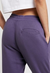 Lila sweatpants med ribbad midja, som har en rund bakficka. Slät textur med en avslappnad passform, kort topp ovanför.
