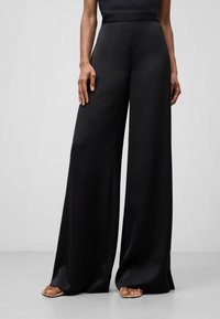 Pantaloni neri a gamba larga realizzati in tessuto morbido. Il design presenta una vita alta e una silhouette fluida, senza motivi o decorazioni visibili.