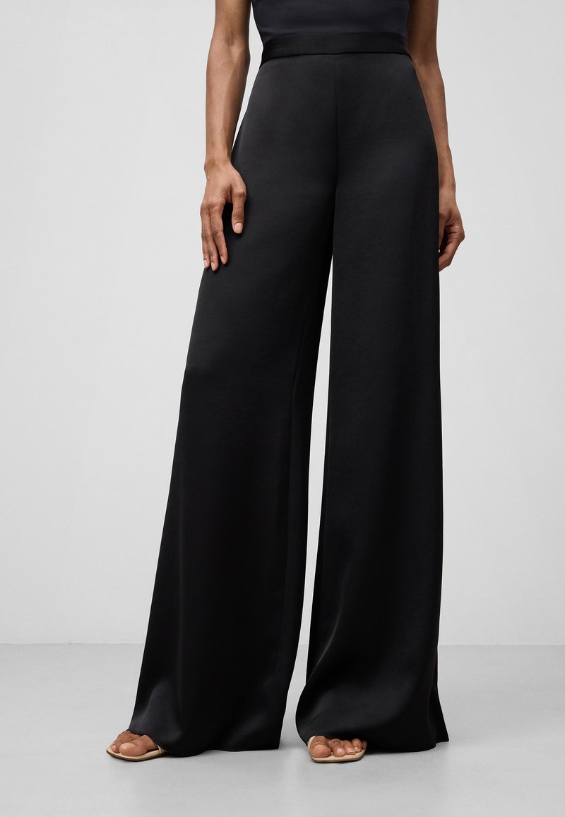 Pantaloni neri a gamba larga realizzati in tessuto morbido. Il design presenta una vita alta e una silhouette fluida, senza motivi o decorazioni visibili.