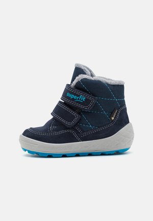 Bottes pour enfants bleu marine avec une doublure grise douce, des bandoulières velcro et une semelle blanche texturée avec des accents bleus ; construction imperméable.