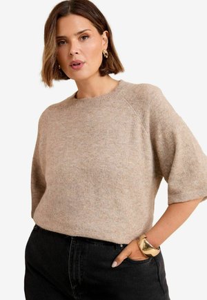 Hellbeige kurzärmliger Strickpullover mit Rundhalsausschnitt, der eine weiche Textur und einen lässigen Schnitt aufweist. Kombiniert mit schwarzen hochgeschnittenen Jeans.