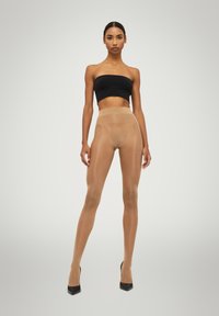 Nude genomskinliga strumpbyxor med hög midja, mjuk textur och matchande nyans, tillsammans med svarta högklackade skor och en svart crop top.