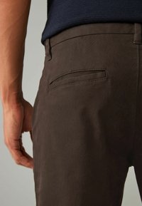 Smeđe hlače s teksturiranim završetkom, s jednim stražnjim džepom i slim fit dizajnom. Boja je jednobojna bez vidljivih uzoraka ili hardvera.