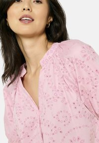 Rozā izšūtā blūze ar ziedu rakstiem, pogu apkakli un savelkošiem detalizējumiem uz piedurknēm. Gluda auduma tekstūra.