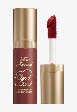 Too Faced Cloud Crush Whipped Lip und Cheek Color in einem roten Tube mit einer goldenen Kappe, die mit einem Herzakzent verziert ist, sowie einem weißen Applikatorstab.