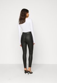 Zwarte faux leren skinny broek met een hoge taille, voorzien van achterzakken en een gladde textuur, gecombineerd met een wit shirt met lange mouwen.