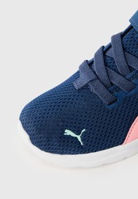 Marinblå mesh atletiska skor med ljusblå detaljer, texturerad ovandel, platta snören och en rosa logotypdetalj på sidan. Gummisula visas.