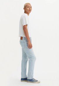 Lichtblauwe spijkerbroek met een rechte snit, gedragen met een wit T-shirt en blauwe sneakers. Leren patch op de tailleband. Strak design.