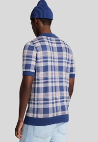 Maglione a maniche corte a quadri in tonalità blu, crema e rosa. Tessuto a maglia con colletto e orlo a costine. Presenta un motivo a scacchi.