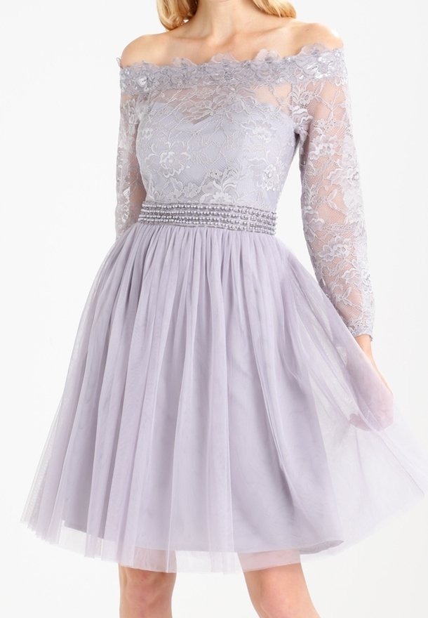 Šaty v levandulové barvě s odhalenými rameny, krajkovým korpusem, průhlednými dlouhými rukávy a plisovanou tylovou sukní. Beadovaný pás přidává detail.