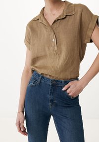 Camicia corta in lino marrone con design a bottoni, abbinata a jeans di denim blu, con una vestibilità classica e tasche laterali.