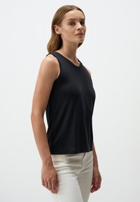 Top nero senza maniche con scollo rotondo, realizzato in tessuto liscio. Presenta una vestibilità regolare e un design semplice, abbinato a pantaloni chiari.