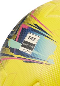 FIFA Quality Pro fodbold i livlig gul med blå og pink geometriske mønstre. Tekstureret overflade og synlig label med produktinformation.