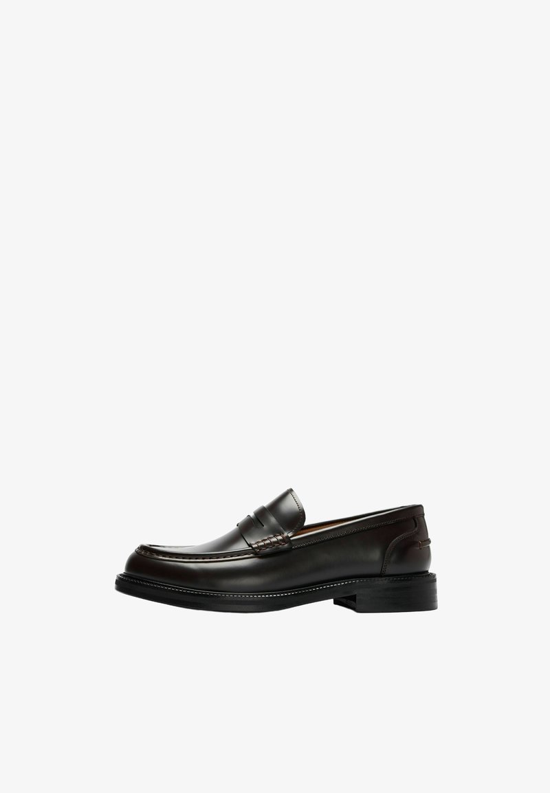 Mocassin en cuir marron foncé avec un petit talon et des détails de couture le long des bords, présenté en profil sur fond blanc.