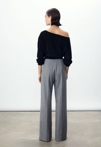 Zwarte off-shoulder trui gecombineerd met grijze wijdvallende broek met krijtstreepjes, met een ontspannen pasvorm en gladde texturen.