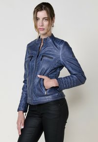 Giacca in pelle blu con collo rialzato, chiusura frontale con zip e quattro tasche con zip. Pannelli texturizzati sulle maniche e ai lati.