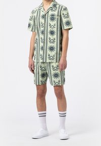 Kurzarmhemd und Shorts-Set in Hellgrün, mit schwarzen Blumen- und Streifenmustern, aus einem leichten Stoff gefertigt. Weiße Sneakers getragen.