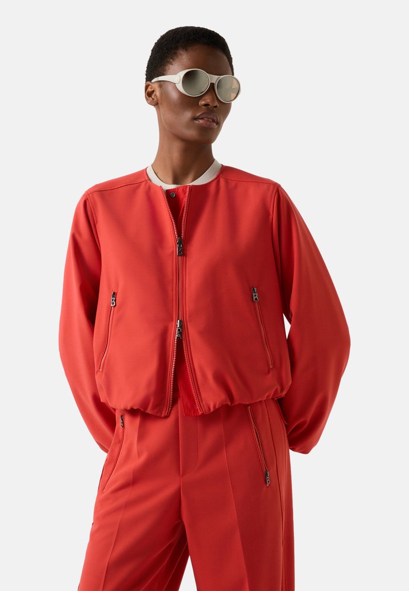 Rød bomberjakke med ribbet krave, lynlåslukning foran og sidelommer. Glat stof, afslappet pasform, kombineret med matchende røde bukser.