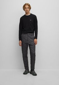 Zwarte long-sleeve shirt met een klein logo, gecombineerd met grijze gewatteerde broek met een textuurpatroon, en zwarte sportschoenen.