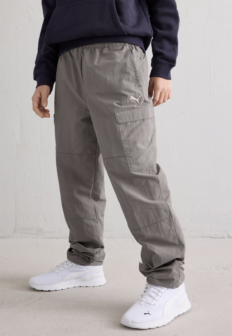 Γκρι cargo παντελόνι με ελαστική ζώνη, πλαϊνές τσέπες και μικρό λευκό λογότυπο Puma. Συνδυασμένο με λευκά αθλητικά παπούτσια.