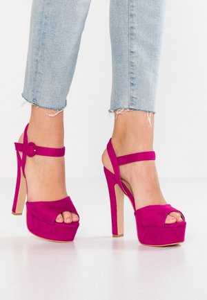 Różowe sandały na wysokim obcasie z odkrytymi palcami, zamszową fakturą, podeszwą na platformie i paskiem wokół kostki z okrągłą sprzączką.