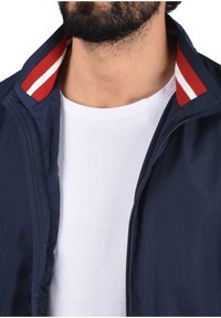 Navy lightweight jacket with red and white striped collar, zippered front, and soft texture, worn over a plain white t-shirt.