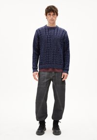 Marine gebreide trui met textuurdesign, ronde hals; grijze broek met hoekige naden, gecombineerd met zwarte veterschoenen.
