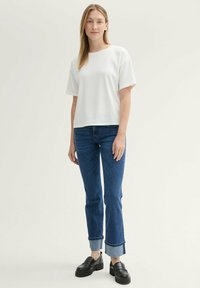 Top blanco de manga corta con superficie texturizada, combinado con jeans rectos azules con dobladillos y zapatos de plataforma negros.