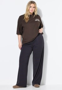 T-shirt marrone oversize con il testo "Friday Coffee", abbinato a pantaloni larghi a righe blu navy. Il materiale sembra morbido e informale.