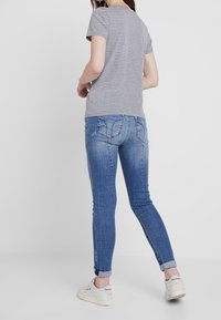 Randig grå t-shirt tillsammans med blå smala jeans, med uppvikta fållar och subtila detaljer på bakfickorna. Vita sneakers fulländar looken.