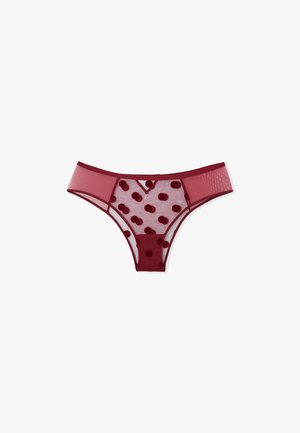 Tanga in rete rossa con pannelli trasparenti, caratterizzato da un motivo a pois di un rosso più scuro. Fascia in vita liscia, design minimalista e senza hardware visibile.