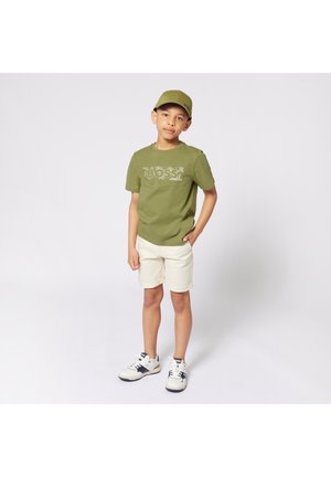 Chemise vert olive avec le logo "BOSS", shorts beiges et baskets blanches avec des accents bleu marine. La casquette assortit la couleur de la chemise.