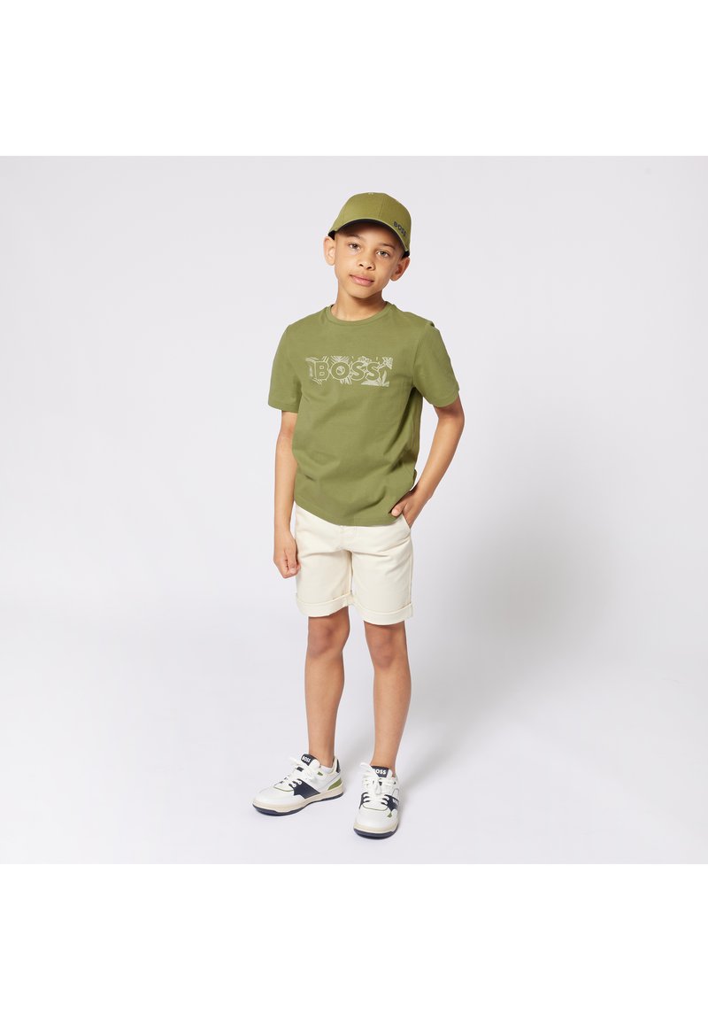 Olivengrønn skjorte med "BOSS"-logo, beige shorts og hvite sneakers med marineblå detaljer. Kappen matcher skjortefargen.