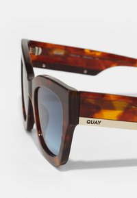 schildpad zonnebril met een chunky rechthoekig montuur, gradient lenzen en gouden accenten aan de zijkanten met het "QUAY" logo. Gelaagde afwerking.