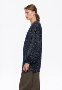 Granatowy, oversize'owy sweter dziany z teksturowanej tkaniny, z błyszczącymi akcentami i balonowymi rękawami. W zestawieniu z oliwkowymi spodniami.