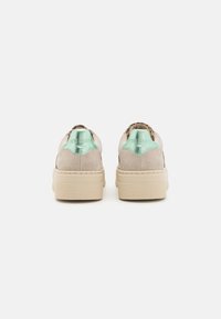 Beige Wildlederschuhe mit einer strukturierten Plattformsohle, ausgestattet mit einem mintgrünen Akzent an der Ferse und einem braun gemusterten Innenraum.