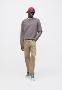 Sweat-shirt gris, pantalon beige et baskets bleues. Casquette rouge et lunettes de soleil. Tenue décontractée avec tissu texturé. Design minimaliste.