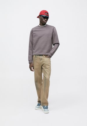 Sweat-shirt gris, pantalon beige et baskets bleues. Casquette rouge et lunettes de soleil. Tenue décontractée avec tissu texturé. Design minimaliste.