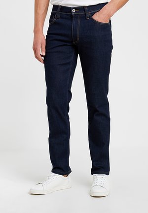 Donkerblauwe jeans van denim met een slim fit, vijf zakken, contrasterende stiksels en een knoopsluiting, gecombineerd met witte sneakers.