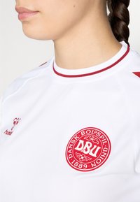 Valge sportlik särk punaste rõhutustega, ümarate kraega, logo rinnal ja struktuurne kangas hingavuse tagamiseks.
