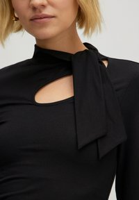 Schwarzes Langarmoberteil mit einer Schleifenverschluss am Hals, Cut-Out-Detail auf der Brust und weichem, glattem Stoff. 