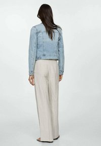 Lyseblå denimjakke med cropped snit, synlige stikninger og knapdetaljer, parret med grå stribede bukser med bred ben.