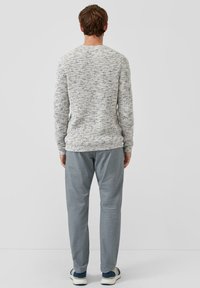 Weißer Strickpullover mit blauen Sprenkeln, Rundhalsausschnitt und geripptem Saum, kombiniert mit hellgrauer Hose und weißen/blauen Sneakers.