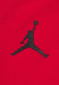Tessuto rosso con un silhouette ricamato in nero di un giocatore di basket in salto, che tiene una palla. Il design enfatizza il movimento atletico.