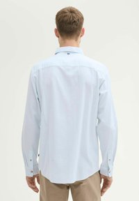 Lichtblauw overhemd met lange mouwen, gezien van de achterkant. Heeft een button-down kraag, een gestructureerde stof en knoopmanchetten. Subtiele branding bij de nek.