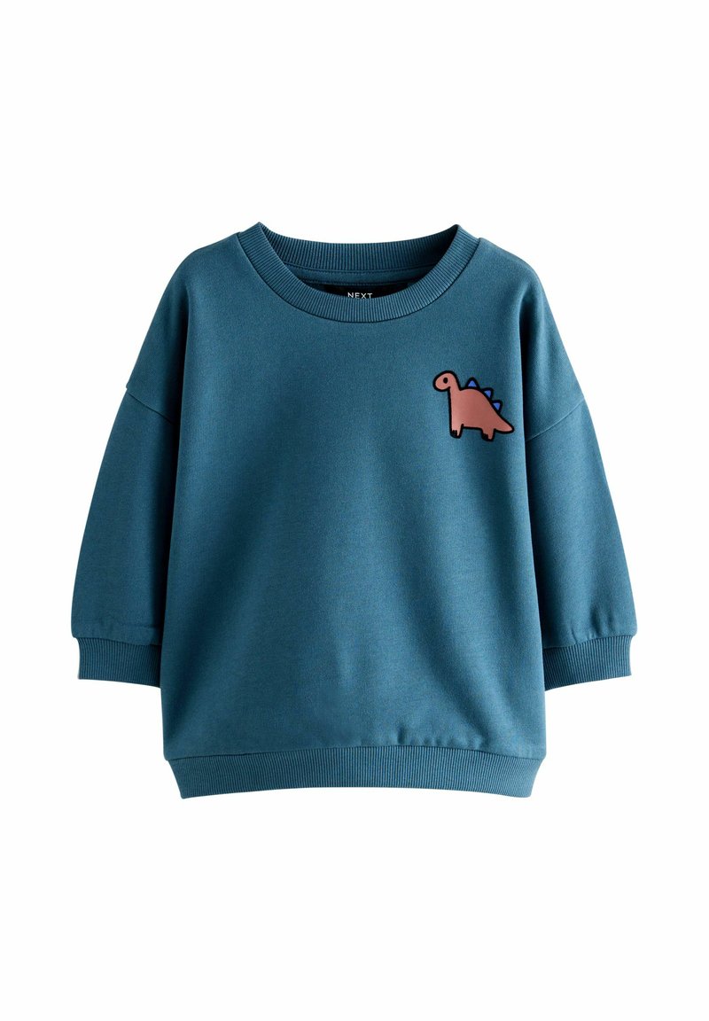 Felpa blu per bambini con una patch di un dinosauro cartone animato rosa sul lato sinistro del petto e polsini e orlo a coste.