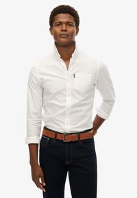 Witte overhemd met knoopsluiting, een klein borstzakje en opgerolde mouwen, gecombineerd met donkere spijkerbroeken en een bruine leren riem.